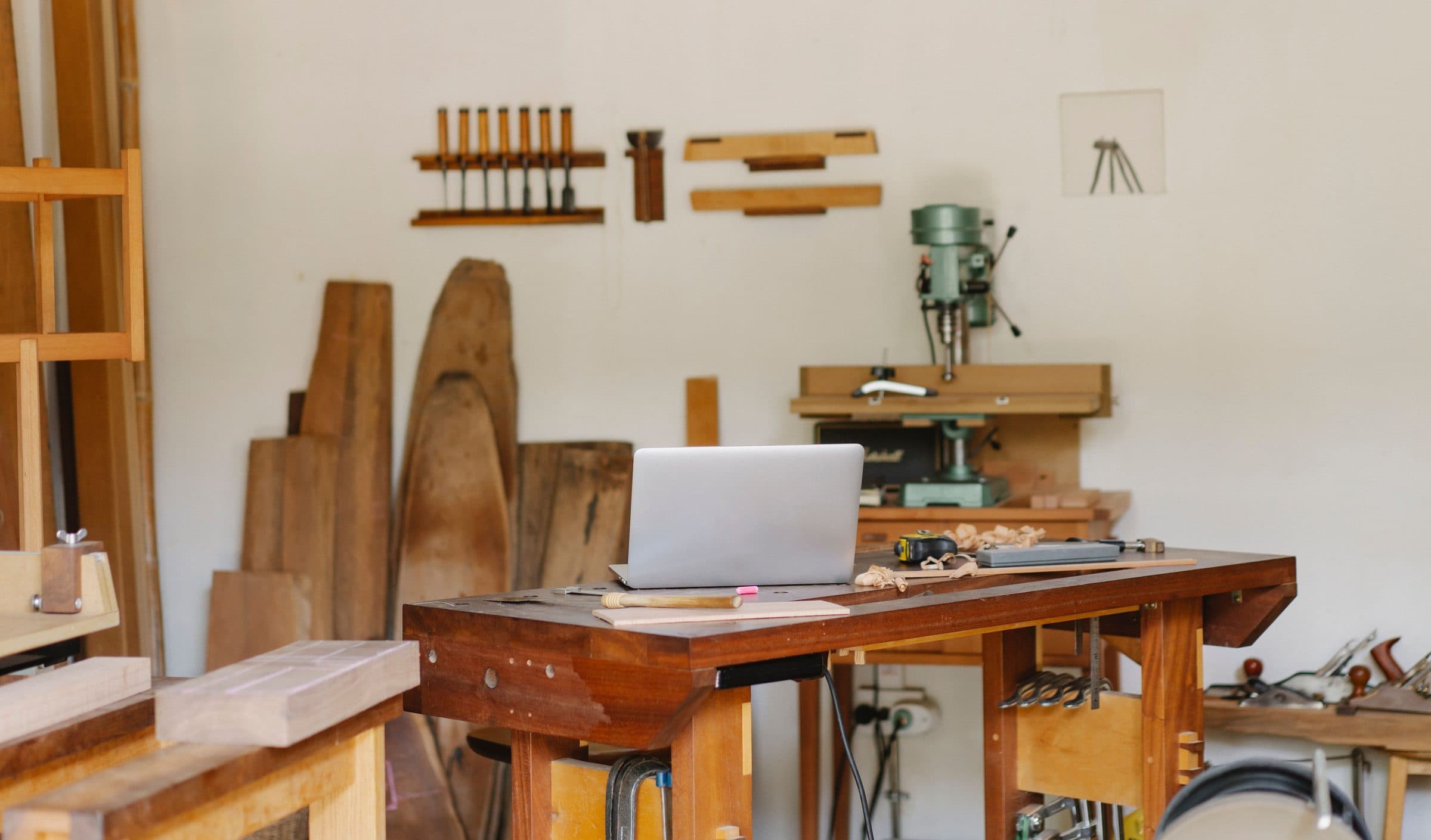 Planches de bois massif dressées contre le mur de l’atelier, près de l’établi et des ciseaux à bois
