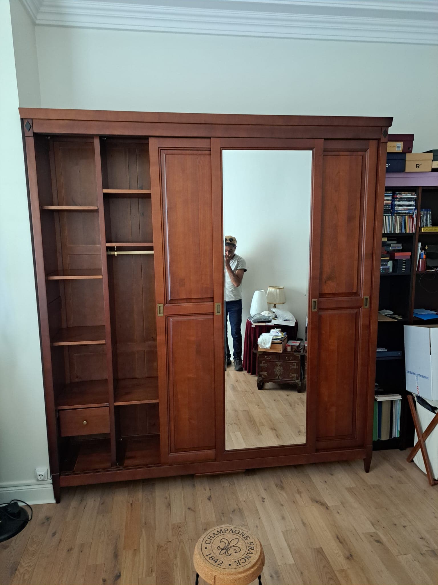 Armoire de chambre en merisier massif à trois portes coulissantes, porte centrale à miroir pleine hauteur, poignées de laiton encastrées, penderie à tringle de laiton et colonne d’étagères