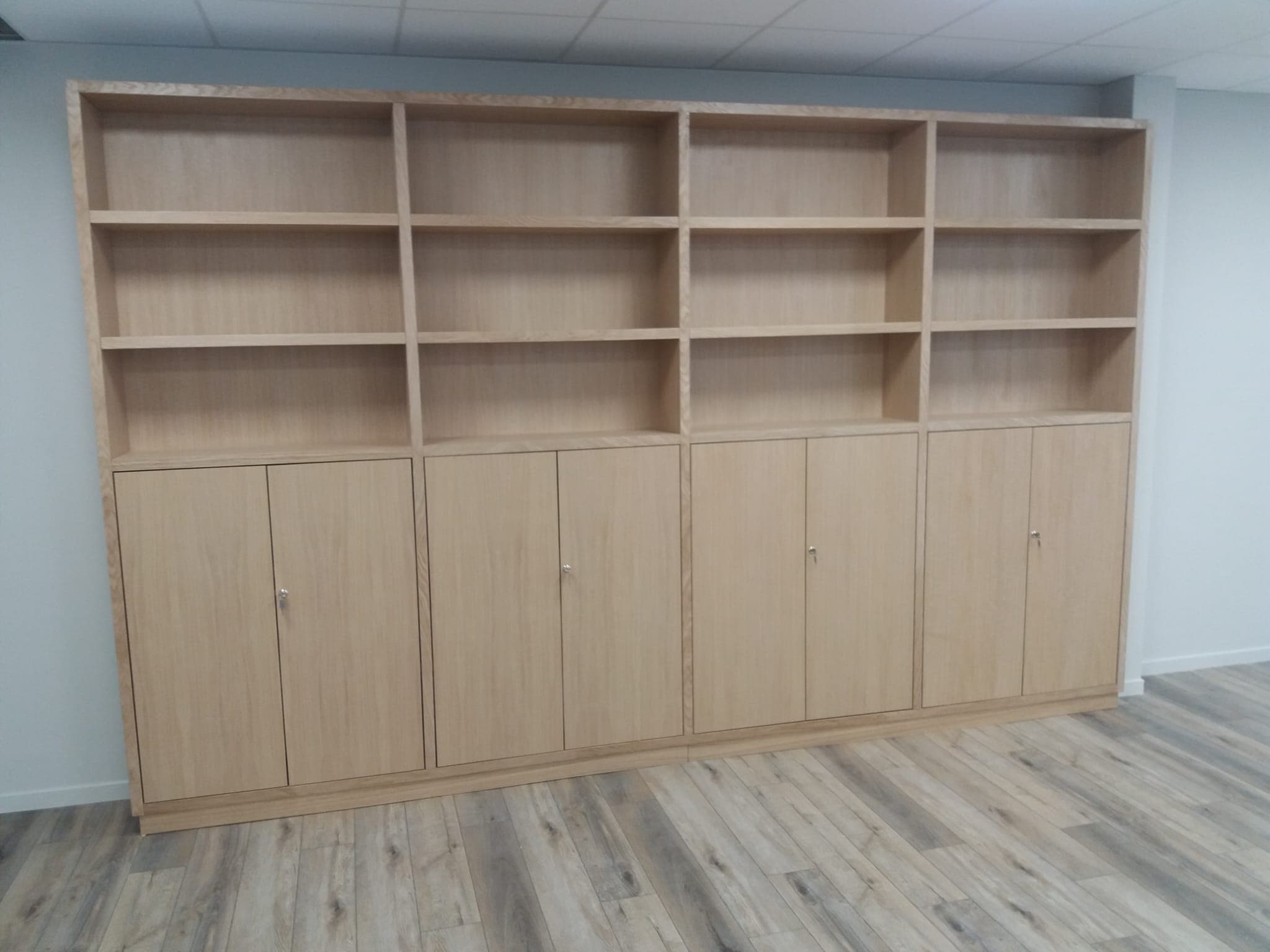 Bibliothèque de bureau de 4 mètres en chêne clair : quatre travées de trois niveaux de rayonnages ouverts au-dessus de huit portes pleines à serrure, socle en retrait