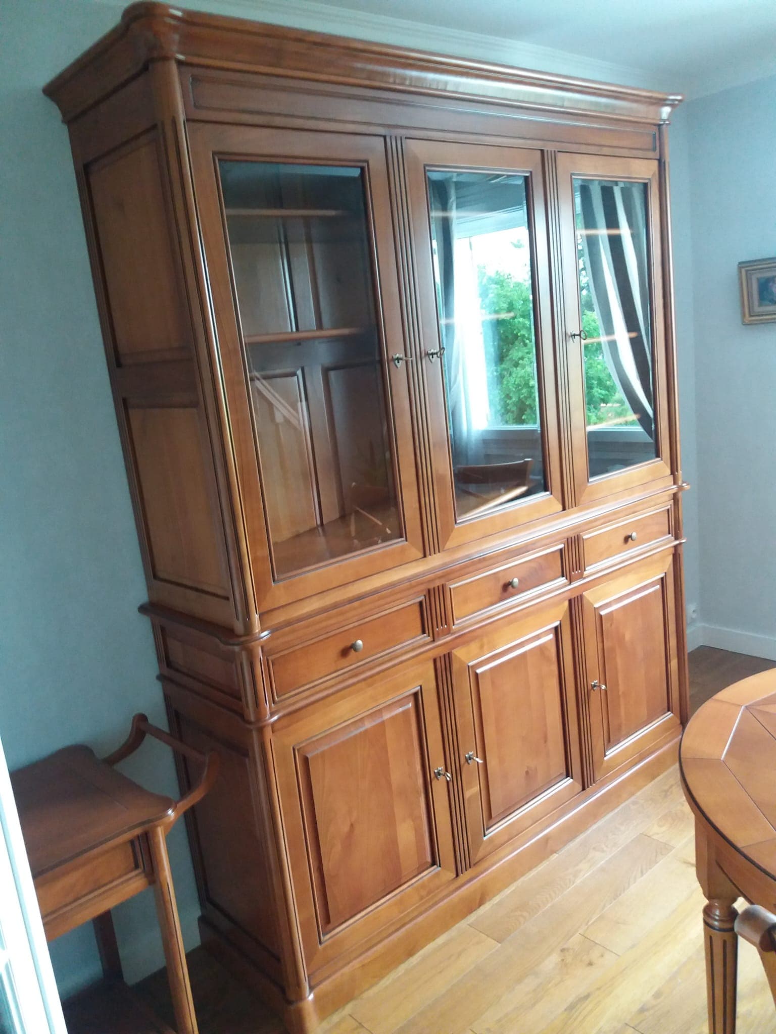 Buffet-vitrine deux corps en merisier massif : trois portes vitrées sur tablettes réglables, trois tiroirs, trois portes à panneaux moulurés en partie basse, côtés menuisés à panneaux et pilastres cannelés