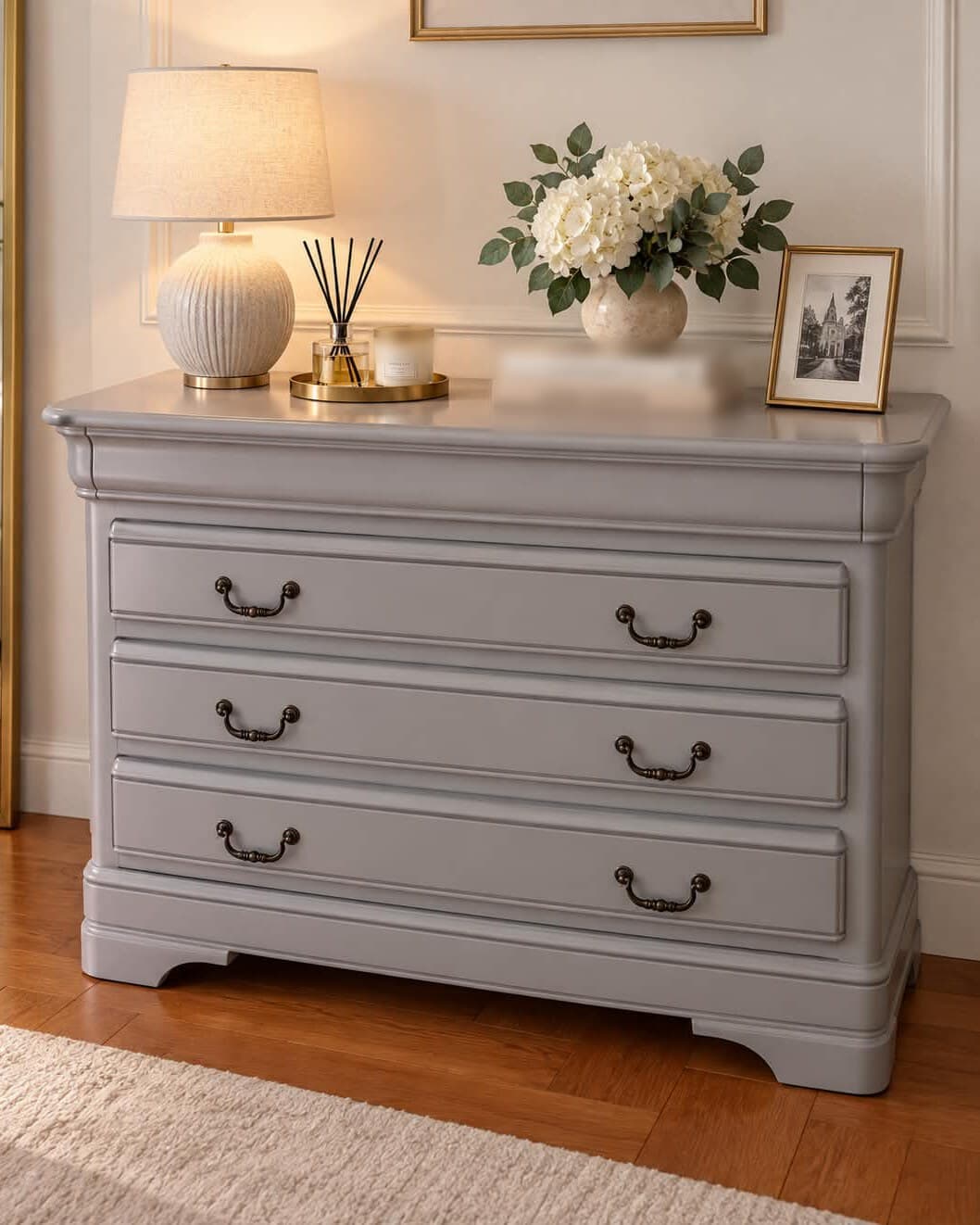 Commode Louis-Philippe laquée grise, plateau aux angles arrondis, ceinture bombée en doucine, trois tiroirs à poignées tombantes en métal patiné et socle à pieds découpés