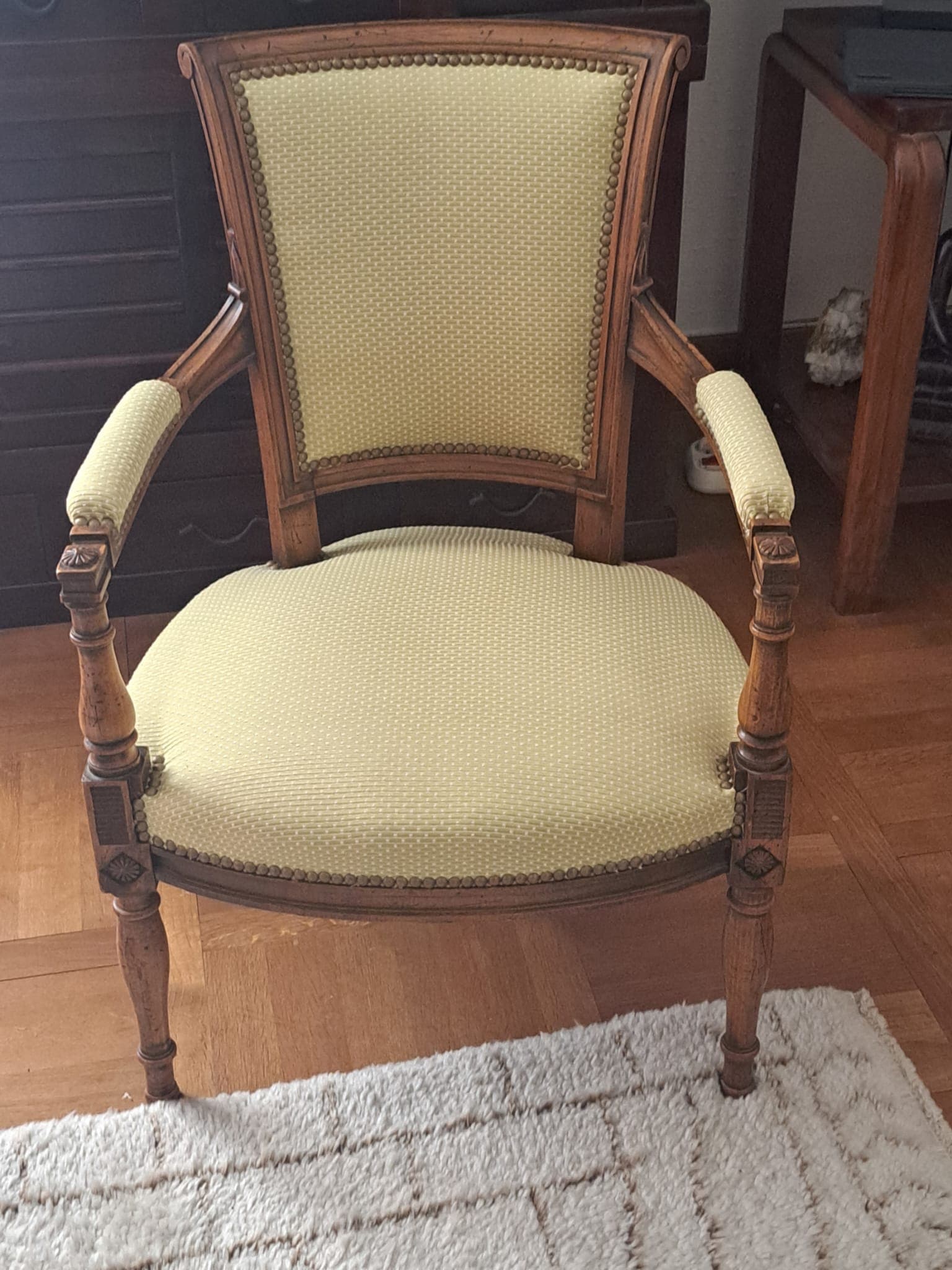 Fauteuil Directoire ancien retapissé en tissu vert amande avec cloutage laiton posé main, dés à rosaces sculptées, sur parquet en point de Hongrie